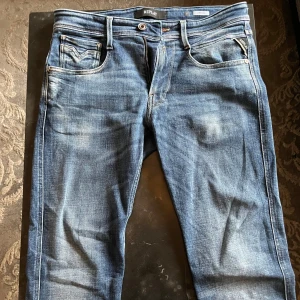 Blå Replay Anbass jeans, storlek 31 - Snygga blå Replay Anbass jeans med klassisk femficksdesign och ljusa slitningar. Jeansen har normal passform, raka ben och detaljerade bakfickor med kontrastsömmar. Perfekta för dig som gillar en avslappnad men stilren look.