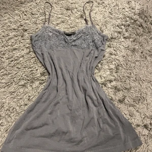 Grå klänning från By Malene Birger - Snyggt grått linne från By Malene Birger med spetsdetaljer upptill. Linnet har smala axelband och en elegant passform. Perfekt för en stilren look.