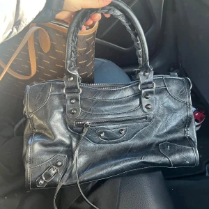 Svart handväska  - Snygg svart handväska i skinn med flätade handtag och flera dekorativa detaljer. Super fin väska som knappt är använd! Köpte för 400, men säljer för 150kr! Inga defekter som jag kan se💕