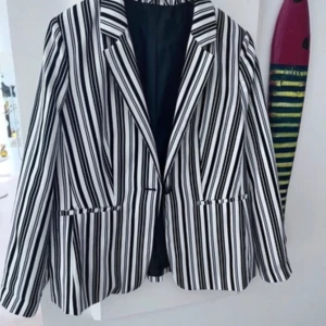 Svartvit randig kavaj - Snygg svartvit randig kavaj med klassisk krage och långa ärmar. Kavajen har en stilren design med knappar framtill och fickor på sidorna. Perfekt för en chic och modern look.