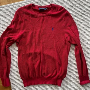 Röd tröja från Polo Ralph Lauren - Säljer en snygg röd tröja från Polo Ralph Lauren i mjuk bomull. Tröjan har en klassisk design med rund hals och långa ärmar. Den ikoniska loggan är broderad i blått på bröstet. Perfekt för en stilren look!