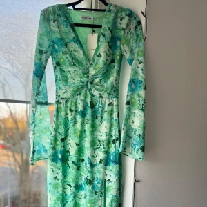 Grön blommig klänning från Adoore - Säljer en vacker grön långklänning från Adoore med blommigt mönster. Klänningen har en v-ringad design och långa ärmar. Perfekt för vårens och sommarens tillfällen. Den har en elegant slits framtill. Helt ny, lappar kvar. Slutsåld på hemsidan💚💚 storlek 32