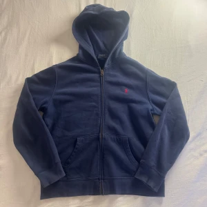 Blå hoodie från Ralph Lauren - Säljer en snygg blå hoodie från Ralph Lauren med dragkedja och huva.💫 Den har en liten röd logga på bröstet och praktiska fickor framtill. Perfekt nu till våren och sommaren 2025! Nypris - (2400 kr) Säljer nu för 479 eftersom tröjan använts ett antal gånger. Armlängd  = 67cm (från sidan av halsen till handleden) Längd på hoodie = 50cm (Från axel till midja) Inga returer! ⭐️