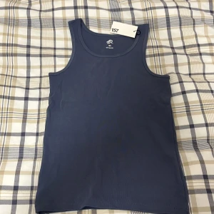 Mörkblå linnetopp från 157 - Säljer en mörkblå linnetopp från 157 i 100% ekologisk bomull. Perfekt för varma dagar med sin ärmlösa design och mjuka material. Enkelt och stilrent plagg för en avslappnad look.Inte använd.🌟