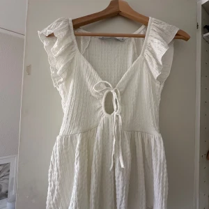 Vit blus med knytning från Lager 157 - Säljer en söt vit blus med volangärmar och knytning framtill. Blusen har en v-ringad design och är perfekt för varma dagar. Den är tillverkad i ett lätt och luftigt material.