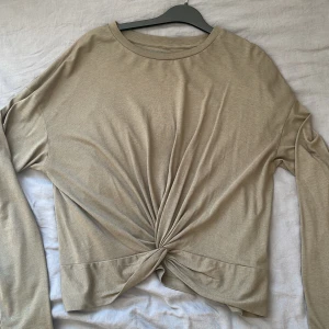 Beige långärmad topp från Noisy May - Säljer en grön långärmad topp från Noisy May. Toppen har en unik knutdetalj framtill som ger en snygg twist. Perfekt för en stilren look.
