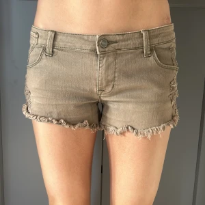 Gröna jeansshorts med fransar LÅGMIDJADE! - Snygga gröna jeansshorts med fransiga kanter och klassisk femficksdesign. Perfekta för en avslappnad sommarlook. De har en knapp och dragkedja framtill.