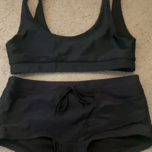 Svart bikini med knytning - Snygg svart bikini med sportig topp och shorts med knytning i midjan. Perfekt för en dag på stranden eller vid poolen. Enkel och stilren design som passar alla tillfällen. (Överdel är i S och underdelen är 36)
