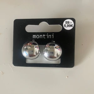 Silverfärgade örhängen från Montini - Snygga och stilrena silverfärgade örhängen från Montini. Perfekta för att ge en elegant touch till din outfit. De är runda och blanka, vilket gör dem till ett tidlöst val för alla tillfällen.