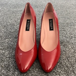 Röda pumps från Tiger of Sweden - Snygga röda pumps från Tiger of Sweden i lackat material. De har en elegant spetsig tå och en stabil klack som ger en stilren look. Perfekta för att lyfta vilken outfit som helst. Aldrig använt.