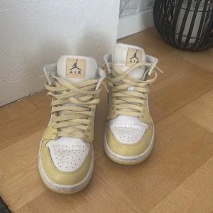 Nike Air Jordans i gult och vitt - Säljer ett par Nike Air Jordans i en fräsch kombination av gult och vitt med blå detaljer. Skorna har klassisk snörning och den ikoniska Air Jordan-loggan på sidan. Perfekta för dig som vill ha en stilren och sportig look.