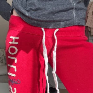 Röda lågmidjade mjukisbyxor från Hollister - Snygga röda mjukisbyxor från Hollister med vit snörning i midjan och tryckt logga längs benet. De är väldigt lågmidjade!! Midjan är 36cm rakt över och innerbenslängden är ca 82cm♥️♥️