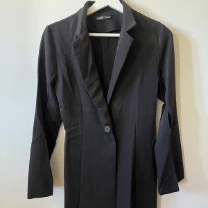 Svart kavajblus - Svart kavaj/blus med en knapp där fram. Slits över armen. 