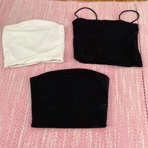 Svart och vit tubtopp - Säljer två svarta och en vit tubtopp. En av de svarta topparna har smala axelband medan de andra är axelbandslösa. Perfekta för sommardagar eller som basplagg i garderoben.