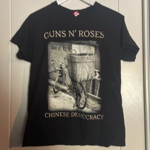 Svart Guns N' Roses t-shirt - Cool svart t-shirt med Guns N' Roses 'Chinese Democracy' tryck. Perfekt för rockälskare! T-shirten har korta ärmar och är gjord av bomull för en bekväm passform.