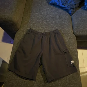 Svarta shorts från Nike - Säljer ett par svarta shorts från Nike med elastisk midja och en praktisk ficka på sidan. Perfekta för en avslappnad stil.