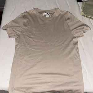 Beige t-shirt från These Glory Days - Säljer en stilren beige t-shirt från These Glory Days. Den har en klassisk rund hals och korta ärmar, perfekt för en avslappnad look. Passar bra till både jeans och shorts.