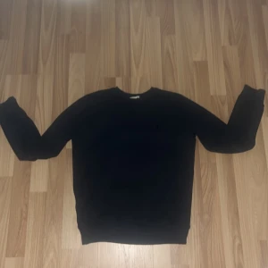 Svart tröja från Ralph Lauren - Säljer en stilren svart tröja från Ralph Lauren med det klassiska logotypbroderiet på bröstet. Tröjan har långa ärmar och en rund halsringning. Perfekt för en avslappnad men ändå elegant look.