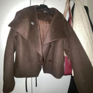 Brun kappa från Gina Tricot - Snygg brun kappa från Gina Tricot med stora slag och knappar framtill. Perfekt för kyligare dagar med sin stilrena design och bekväma passform.