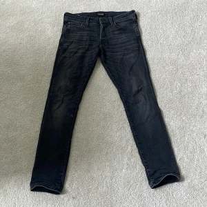 Svarta slim jeans från Jack & Jones - Säljer ett par svarta slim fit jeans från Jack & Jones, modell Glenn. Jeansen har en snygg tvättad look med diskreta slitningar och klassiska fem fickor. Materialet är stretchigt jeans för extra komfort. 32 x 32