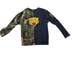 Camo och marinblå tröja från Polo Ralph Lauren - Unik crewneck från Polo Ralph Lauren med halva tröjan i camouflage och andra halvan i marinblått. Stor gul tigerpatch framtill och broderade märkesdetaljer på ärmarna. Långärmad och i mjuk bomull, perfekt för dig som vill sticka ut.