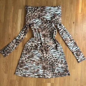 Leopardo klänningen  - Snygg kortklänning från Monki i storlek XS med coolt mixat leopard- och zebramönster i brunt, svart och vitt. Klänningen har långa ärmar och offshoulder-modell som ger en trendig vibe.     
