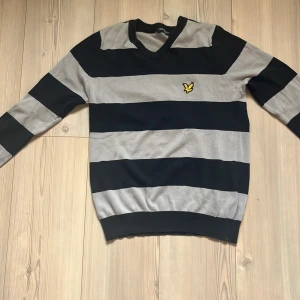 Randig tröja från Lyle & Scott:Vintage, stilig! - Snygg långärmad tröja från Lyle & Scott i svart och grått med breda ränder och klassisk gul logga på bröstet. V-ringad modell i mjuk bomull, perfekt för dig som gillar stilren och sportig vibe.
