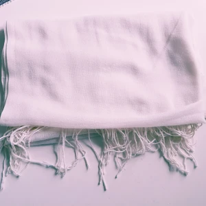 Vit halsduk med fransar - En stilren vit halsduk med långa fransar i kanterna. Halsduken är mjuk och lätt, perfekt att slänga över axlarna för en clean look. Passar dig som gillar minimalistisk stil och vill ha en accessoar som funkar till det mesta. Har 2 likadana  Helt skick dock noppror