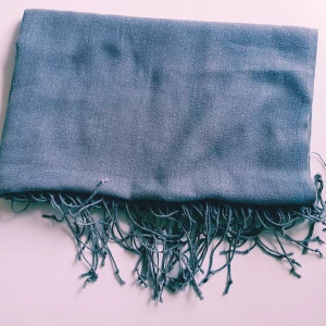 Grå sjal med fransar - En stilren grå halsduk med tunna fransar i kanterna. Sval och mjuk känsla, perfekt att slänga över axlarna för en chill look. Enkel design utan mönster, passar till det mesta och är lätt att styla.  Helt skick dock noppror