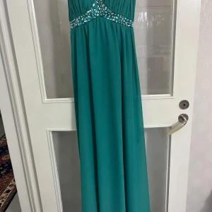 Turkos långklänning med strassdetaljer - Snygg turkos långklänning med smala axelband och glittrande strassdetaljer över bysten och midjan. Perfekt för bal eller festliga tillfällen.