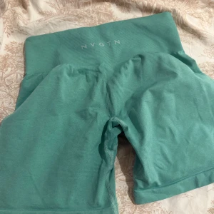 Turkosa träningstights-shorts från NVGTN - Säljer ett par turkosa seamless träningstights-shorts från NVGTN med hög midja och tight passform. Perfekta för gymmet eller löprundan, med stretchigt material som sitter skönt och formar kroppen. Diskret logga framtill på midjebandet.
