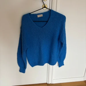 Blå stickad tröja från Freequent - En snygg blå stickad tröja från Freequent med v-ringad hals och långa ärmar. Tröjan har en loose fit med lite ballongliknande ärmar.