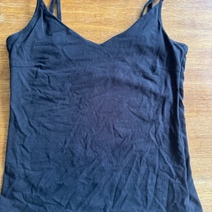 Svart linnetopp från 157, storlek S - En svart, enkel linnetopp från 157 med smala axelband och v-ringad hals. Toppen är gjord i mjuk bomull med lite stretch för en bekväm passform. Perfekt att styla med jeans eller kjol för en clean look.