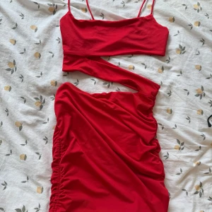 Röd cut-out klänning med smala band - Trendig röd kortklänning med smala axelband och cool cut-out detalj över magen. Klänningen har rynkade sidor och en tight passform som framhäver figuren. Perfekt för dig som vill sticka ut med en färgstark och modern look.