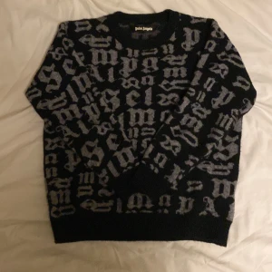 Palm Angels svart stickad tröja - Palm Angels stickad tröja i svart med grått bokstavsmönster över hela plagget. Rund halsringning och långa ärmar. Tröjan har en loose fit och är perfekt för dig som gillar streetwear vibes och vill sticka ut med coola detaljer.