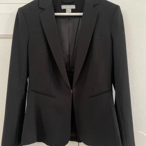 Svart kavaj från H&M, storlek 36 - Klassisk svart kavaj från H&M i storlek 36. Snygg figursydd modell med smala slag, två fickor framtill och knäppning med en knapp🩷Som ny!