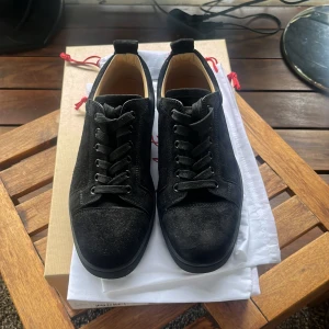 Svarta mockasneakers från Louboutin - Snygga svarta sneakers från Christian Louboutin i mocka med klassisk röd sula och svarta skosnören. Skorna har rund tå och platt sula, samt exklusiv känsla med märkets signaturdetaljer på insidan och undersidan. Perfekta för dig som gillar lyxiga och stilrena sneakers. Dustbag och box tillkommer.
