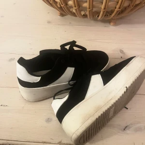 Svarta och vita sneakers från Duffy - Snygga sneakers från Duffy i svart och vitt med chunky plattformsula. Skorna har snörning och en cool kontrast mellan svart ovandel och vita detaljer. Perfekta för dig som vill ha en trendig och bekväm look till vardags.