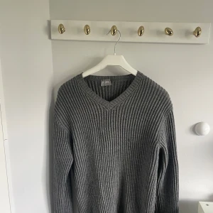  Hugo Boss stickad tröja  - Säljer en grå ribbstickad tröja från Hugo Boss Sport. Tröjan har v-ringad hals, lång ärm och är tillverkad i ett mjukt stickat material. Perfekt för dig som gillar en klassisk och stilren look med lite oversized känsla.