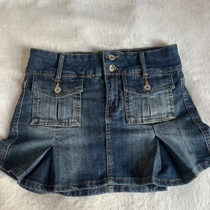 Mörkblå jeanskjol med fickor och volang - Snygg mörkblå jeanskjol med två fickor framtill och dubbla knappar i midjan. Kjolen har markerade sömmar och lätt utsvängd form nertill💓 skriv för fler frågor