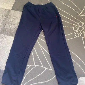 Mörkblå mjukisbyxor från Ralph Lauren - Mörkblå mjukisbyxor från Ralph Lauren med klassisk röd broderad logga på höften. Byxorna har elastisk midja och är tillverkade i mjukt bomullsmaterial, perfekta för chill dagar eller när du vill vara bekväm men ändå se snygg ut.