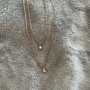 Guldigt dubbelt halsband - Guldigt dubbel halsband med mån berlock och sten berlock. Färgen har ändrats lite men ser fortfarande fin ut. Färgen på haken har rostat.