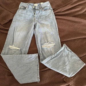 Ljusblåa wide jeans med slitningar - Ljusblå jeans med hög midja och knäppning framtill. Modellen är wide med raka, vida ben och slitna detaljer vid knäna för en cool, avslappnad look. Klassisk femficksdesign och tillverkade i jeansmaterial.