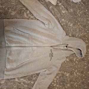 Grå hoodie från Peak Performance - Ljusgrå hoodie från Peak Performance med dragkedja och huva. Tröjan har två stora fickor framtill och diskret logga på bröstet. Har nån hål men säljer för att jag inte använder den längre.