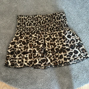 Leopardmönstrad volangkjol - Supersöt kort kjol med leopardmönster och volanger. Kjolen har bred smock i midjan för en bekväm passform och är perfekt för dig som vill sticka ut. Färgerna går i beige, brun och svart. Materialet känns lätt och luftigt. Hittar inte storlek men har för mig att det är i storlek L men passar någ även M