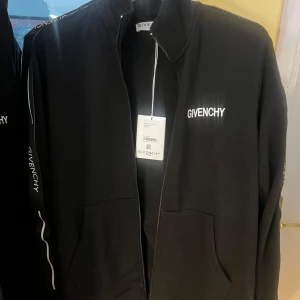 Svart givenchy dress! - Svart dress från Givenchy med vit logga på bröstet och längs ärmarna. Jackan har hög krage, dragkedja framtill och två stora fickor. Tillverkad i mjuk bomull, perfekt för en clean och stilren look.