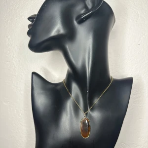 Elegant halsband i rostfritt stål m äkta tigeröga - ädelsten / natursten som symboliserar styrka och skydd - Oanvänt halsband med ett skimrande hänge i äkta tigeröga, infattat i guldfärgad metall. Stenen skiftar vackert mellan bruna och gyllene toner. Kedjan är i guldfärgat rostfritt stål (märkt S. STEEL), hållbar och allergivänlig. Tigeröga sägs vara en skyddande sten som stärker mod, fokus och inre balans – ett perfekt smycke både till vardag och fest. Kedjan är ca 45 + 5 cm, hänget ca 4,5 cm. Prutning accepteras ej, men jag erbjuder rabatt vid köp av flera saker. Kolla gärna på mina andra annonser!