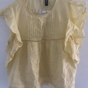 Gul volangblus från H&M - Supersöt ljusgul blus från H&M som är storlek M/38 med volangdetaljer längs ärmarna och fina veck framtill. Blusen är ärmlös och har en luftig passform, perfekt för varma dagar. Tillverkad i tunn bomull som känns lätt och fräsch. Rund halsringning och dekorativ söm under bysten. Priset går att diskutera!💕💕