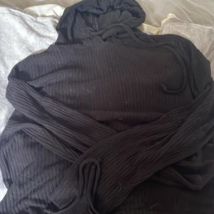 Svart ribbad hoodie med huva - Svart hoodie med ribbad struktur och huva. Tröjan har långa ärmar och dragsko vid huvan för en avslappnad look. Perfekt för dig som gillar en enkel men ändå trendig stil. Materialet känns mjukt och bekvämt mot huden.