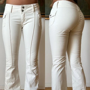 Vita bootcut byxor - Snygga vita byxor med bootcut och markerade pressveck framtill. Byxorna har låg midja, dubbla knappar i linningen och fickor med lock och knapp på sidorna. Trasiga på ett ställa men går för mig att laga hos sömmerska innan jag postar. Materialet är mjukt och stretchigt, perfekt för en clean och fräsch look.